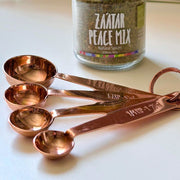 Set of Four Copper Plated Stainless Steel Measuring Spoons next to a spice jar
