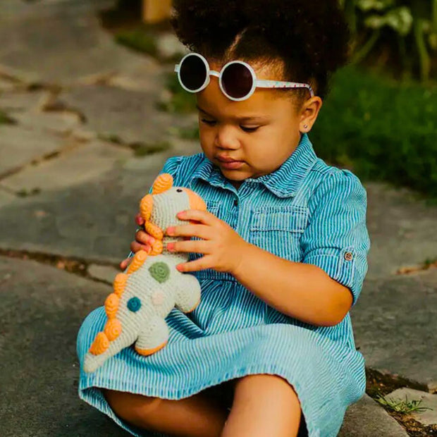 Toddler gift playing with a Pebble Child Hand Crocheted Dinosaur Rattle Toy with orange spikes