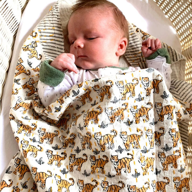 Newborn baby wrapped in a block-printed blanket with tiger pattern, lying on a textured surface.