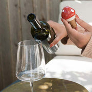 Person pouring wine while holding a hand-painted Mushroom Ceramic Wine Bottle Stopper in the other hand