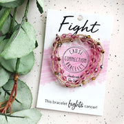 Bracelet with pink beads on a card labeled 'Fight Cause Connection Bracelet' next to green leaves.
