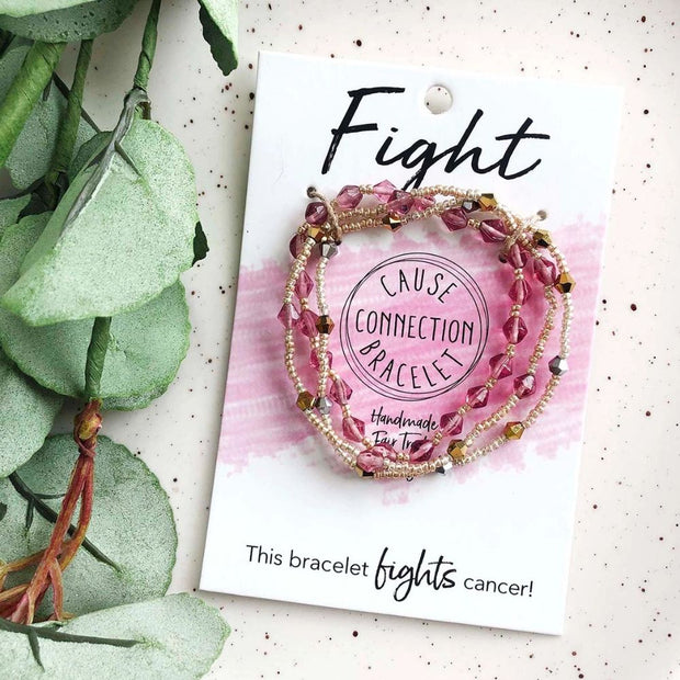 Bracelet with pink beads on a card labeled 'Fight Cause Connection Bracelet' next to green leaves.