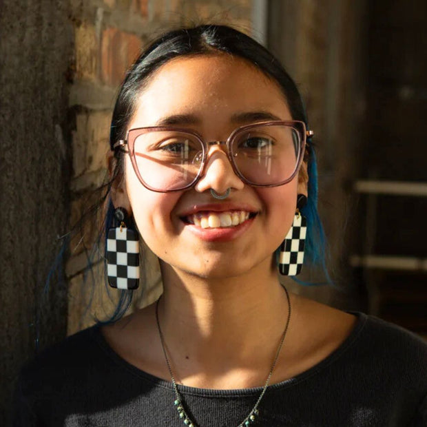 Person wearing a pair of black and white resin checkerboard post earrings