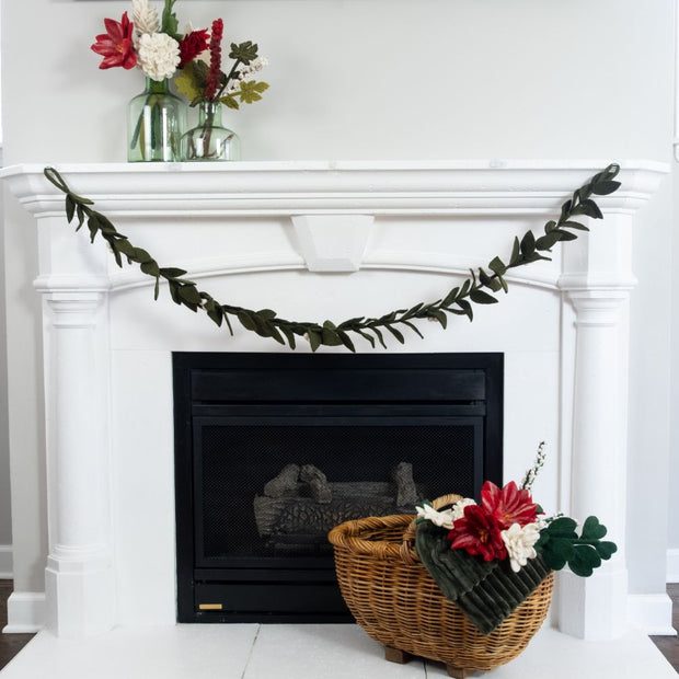 Decorative fireplace with a Fair Trade Felt Mistletoe Garland, basket of felt flowers, and vase of felt flowers on a white mantel.