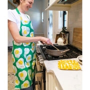 Woman in the kitchen wearing a Reversible Printed Batik Cotton Green Apron with Eggs Print