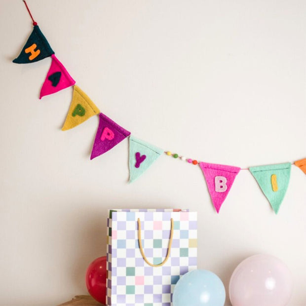 Multicolor Happy Birthday Felt Pennant Banner on a wall with balloons and presents on table