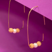 Savvy Hook Wood and Pearl Bead Earrings styled against a dark pink background