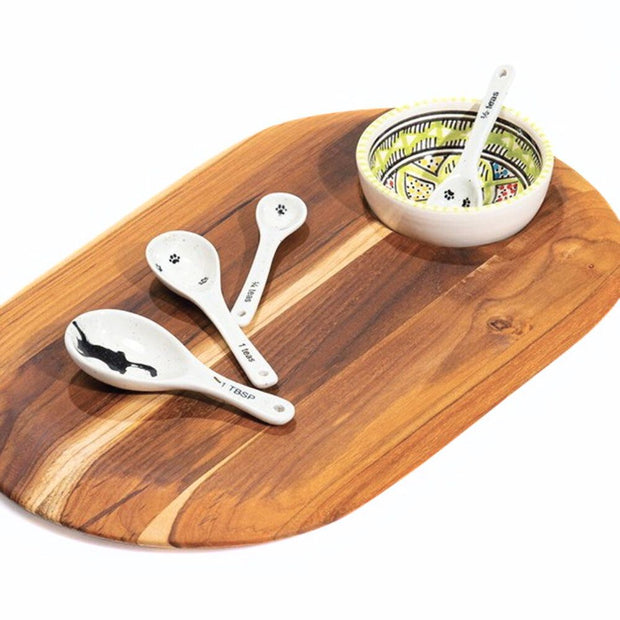 Handmade and Fair Trade Teakwood Oh Oval Cutting Board styled with a round ceramic bowl and measuring spoons