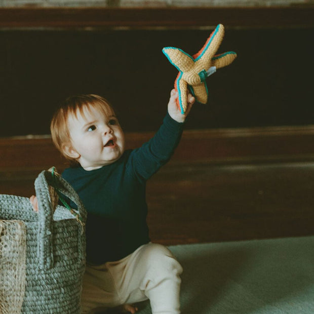 A little boy plays with a Pebble Child Hand crocheted Starfish Rattle